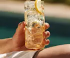 A man holds a whisky highball on his knee while sat next to a pool