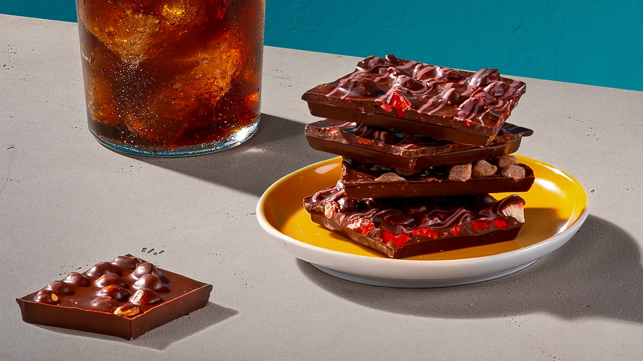 A whisky cocktail next to a plate on which a pile of dark chocolate towers.