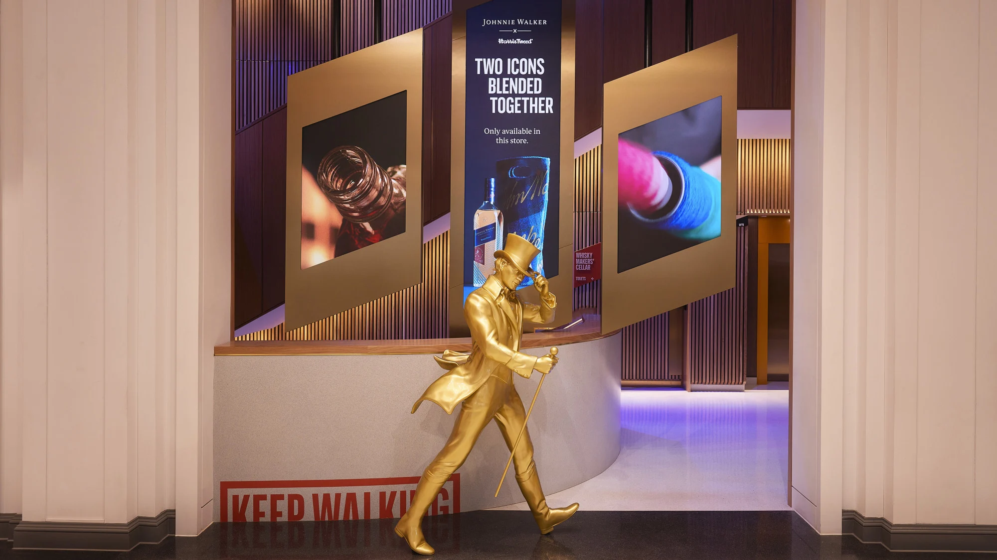 Eine goldene Statue des Johnnie Walker "Striding Man" steht neben einer Theke mit dem roten "Keep Walking"-Logo.    