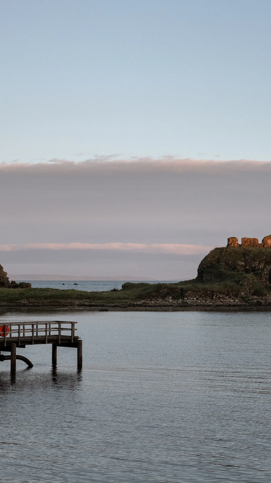 A rocky island outcrop reflected in the calm waters of a sea loch on the Isle of Islay at dusk, with moody skies overhead.
