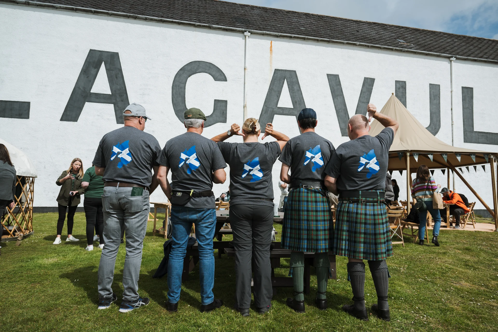 Eine Gruppe von Menschen steht vor der Lagavulin Distillery und zeigt ihre schottische Flagge auf ihren T-Shirts.