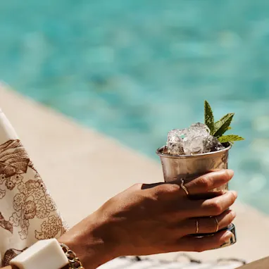 A woman holds a Mint Julep cocktail while sitting next to a pool