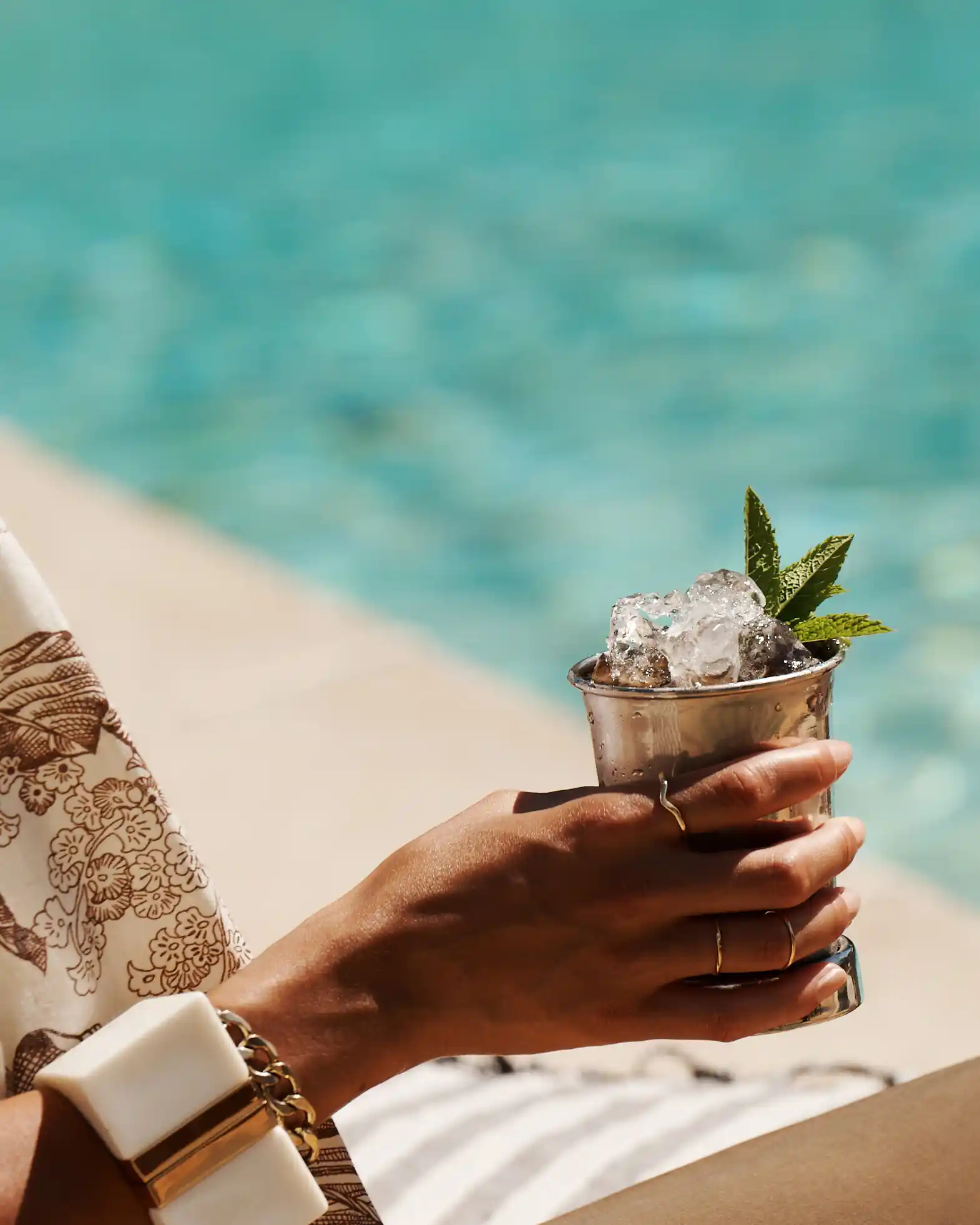 Eine Frau hält einen Mint-Julep-Cocktail in der Hand, während sie an einem Pool sitzt