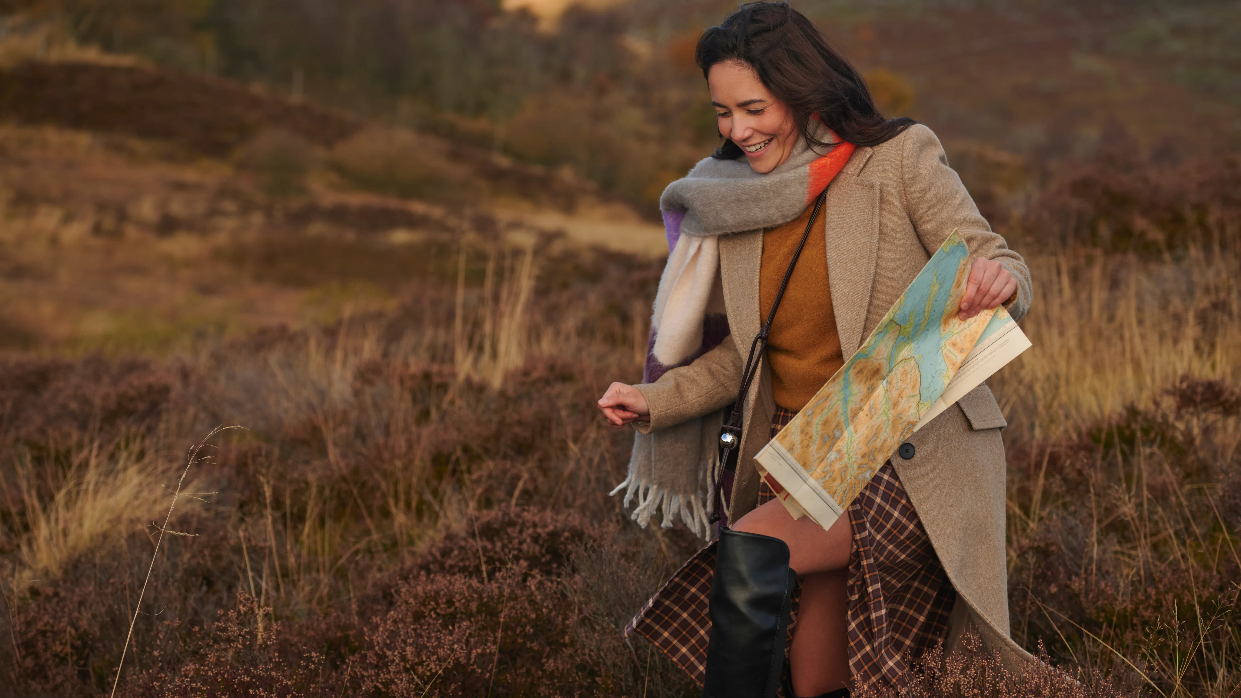 Woman wearing autumnal clothes walking outdoors holding a map.