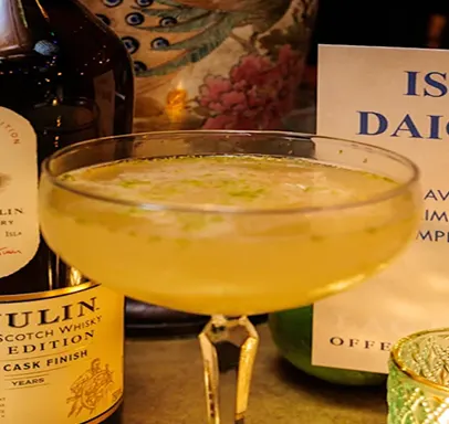 Een close-up van een coupeglas gevuld met Islay Daiquiri cocktail naast een fles Lagavulin whisky.