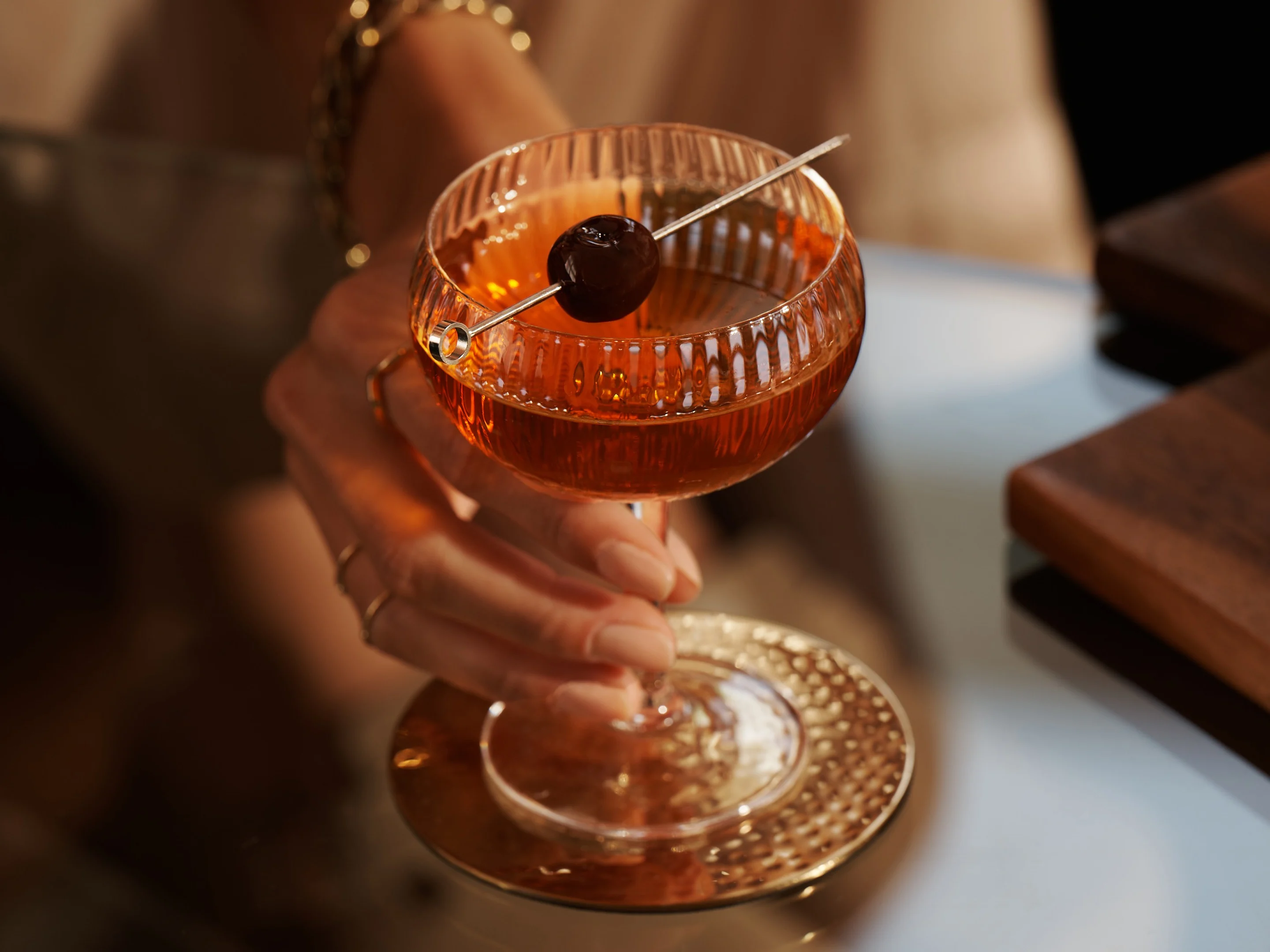 Eine Frau hält einen Manhattan-Cocktail auf einem Glastisch.