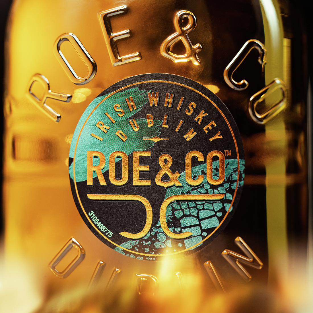 Close-up of the Roe & Co bottle showing the embossed branding and detailed label design in turquoise and gold tones.
