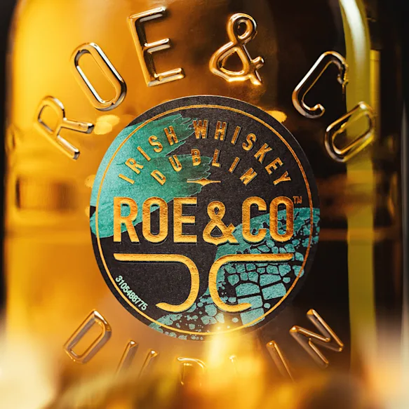 Nahaufnahme der Flasche von Roe & Co mit geprägtem Branding und detailliertem Etikettendesign in Türkis- und Goldtönen.
