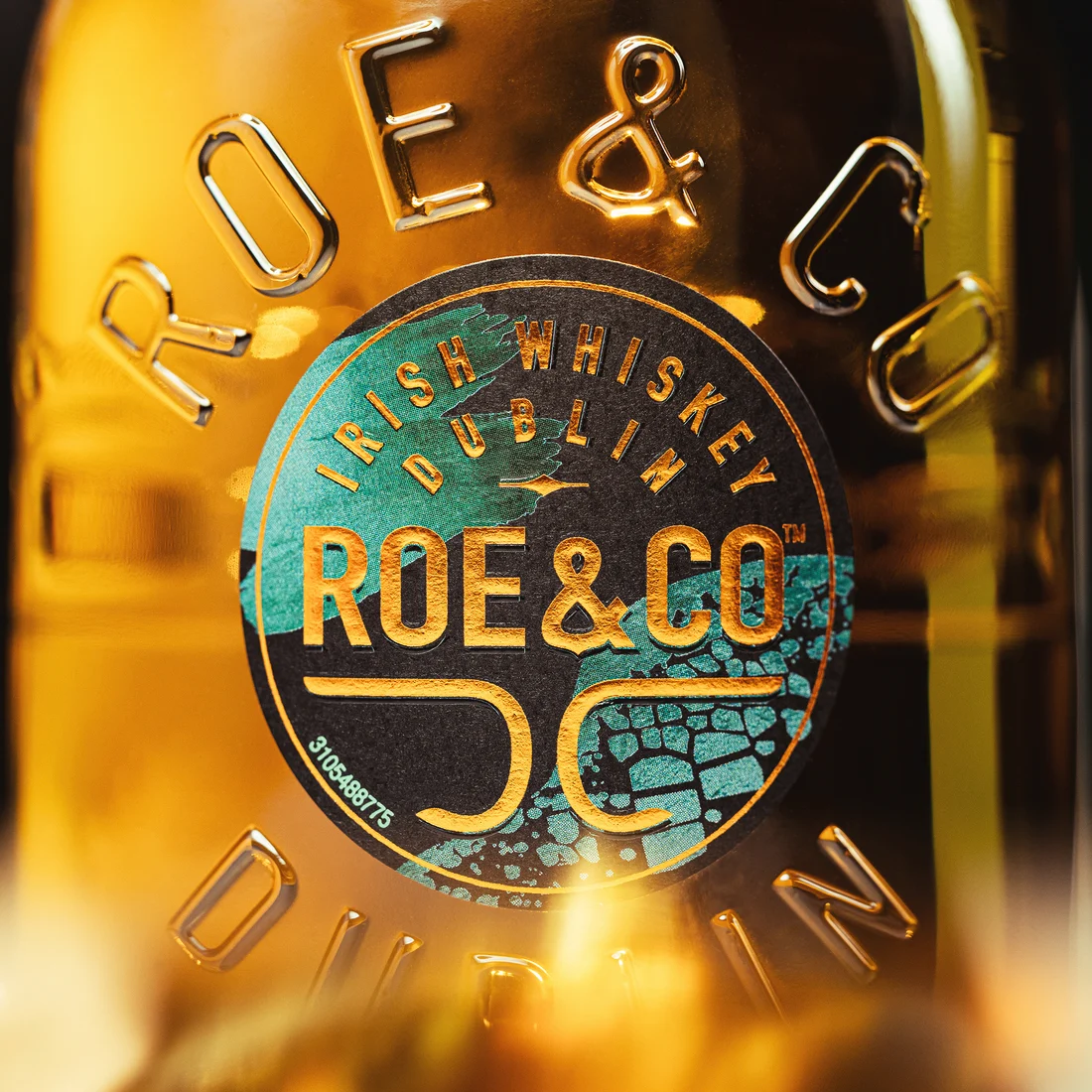 Nahaufnahme der Flasche von Roe & Co mit geprägtem Branding und detailliertem Etikettendesign in Türkis- und Goldtönen.
