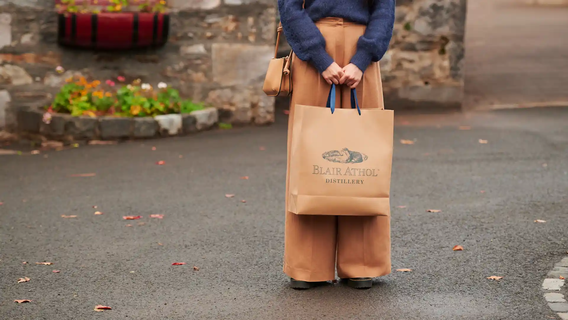 A woman holds a brown paper gift bag which is branded with the Blair Athol distillery logo