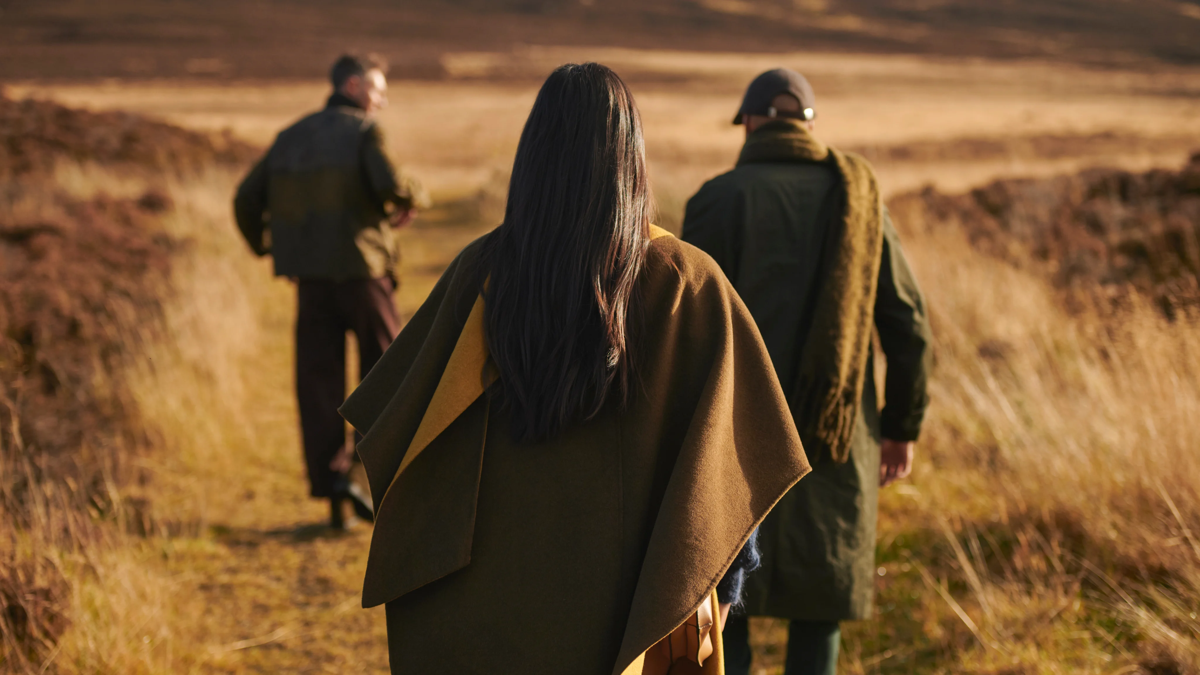 A group of visitors walking across open moorland on the Isle of Islay in autumn, wearing outdoor clothing with rolling hills in the background