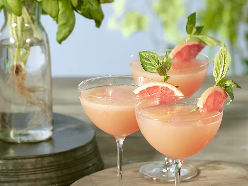 Three Brown Derby cocktails in coupe glasses with pink grapefruit garnishes.