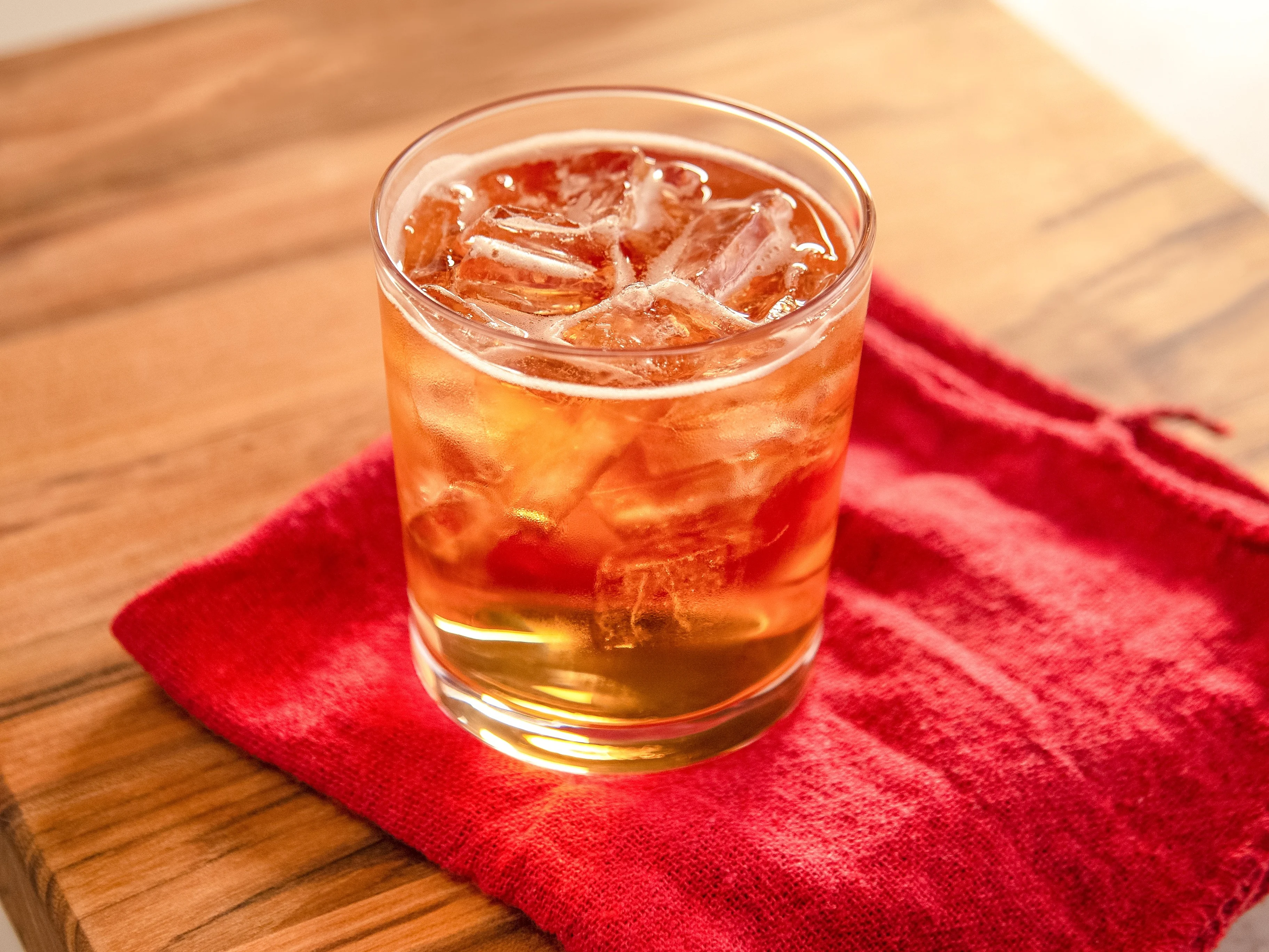 Godfather-Cocktail in einem Glas auf einem Holzbrett mit einer roten Serviette