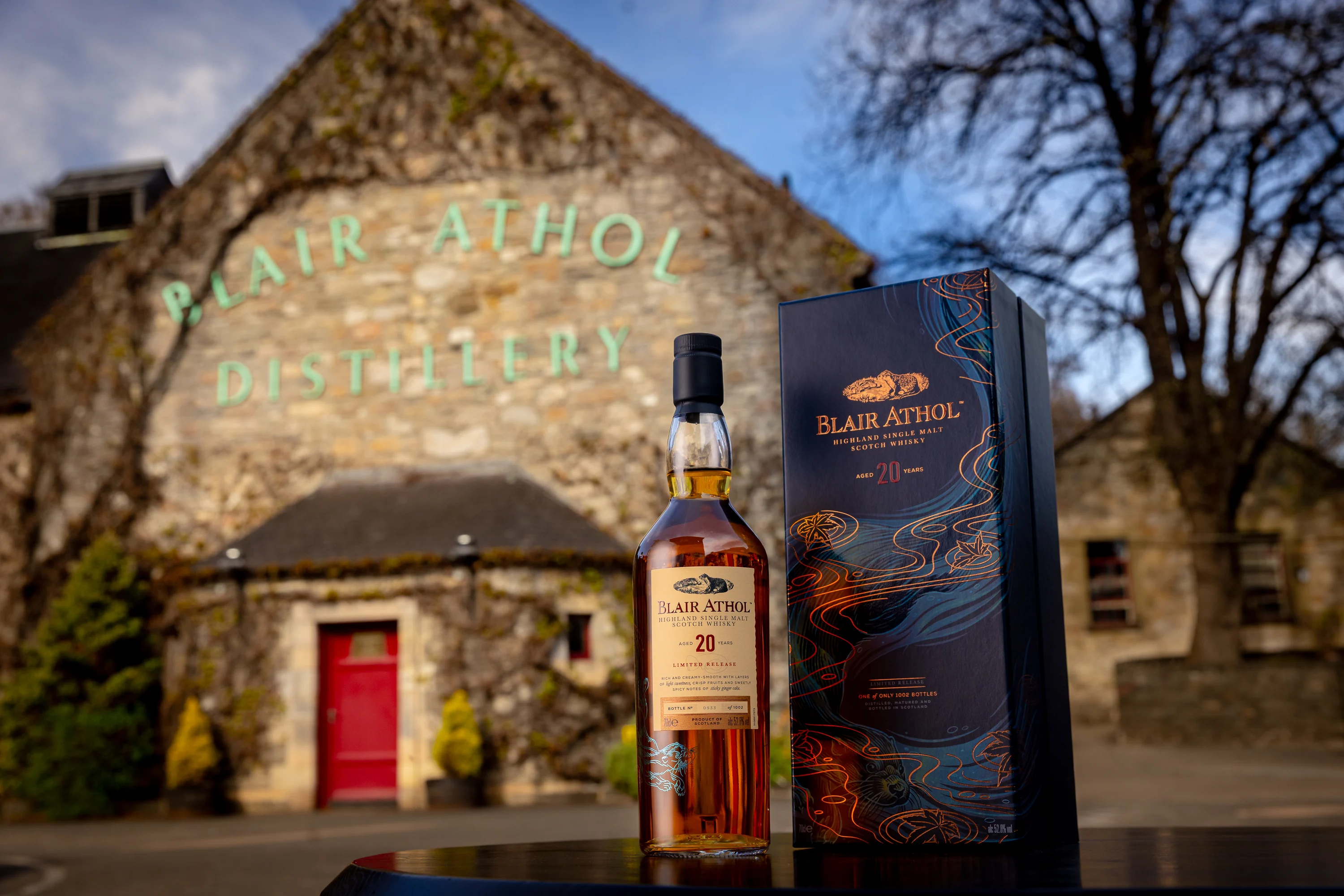 Eine Flasche Blair Athol 20 Jahre alter Highland Single Malt Scotch Whisky mit ihrer Verpackungsbox, präsentiert vor dem historischen Gebäude der Blair Athol Destillerie.