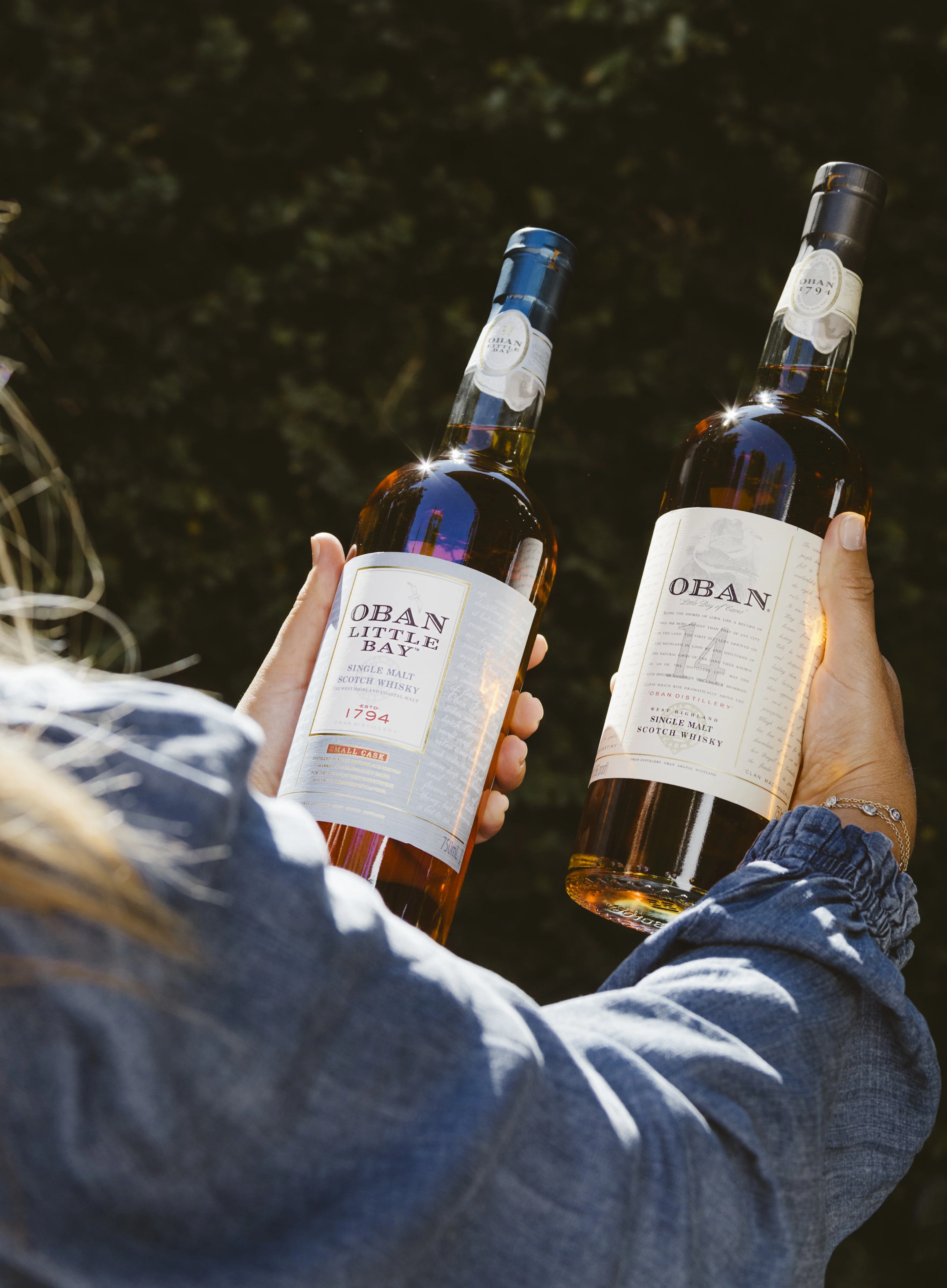 A person holds two bottles of whisky in their hands.