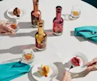 Three bottles of The Singleton Gourmand Collection sit on a white tablecloth, surrounded by three plates of cakes with rocks glasses containing whisky.