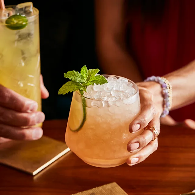 A hand holds a light pink lowball cocktail containing crushed ice and a mint sprig garnish