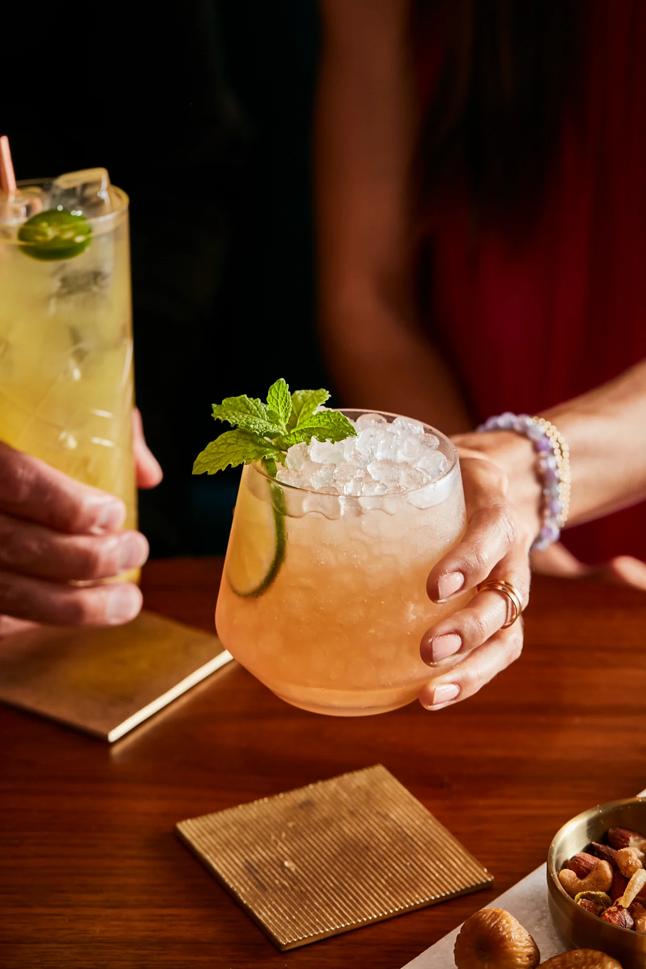 A hand holds a light pink lowball cocktail containing crushed ice and a mint sprig garnish