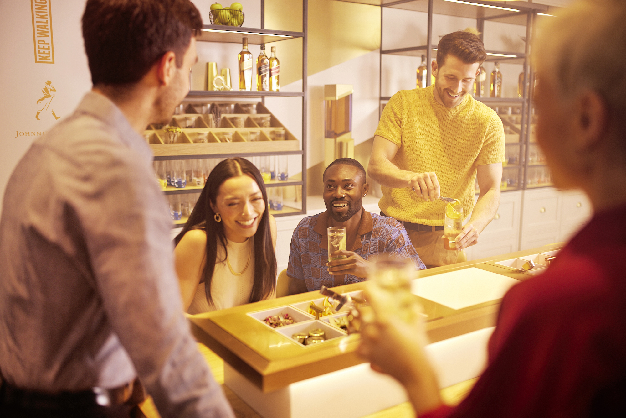 Group of friends doing the Flavour of Journey tour smiling and preparing their highball cocktails while sitting around the table with different cocktail ingredients