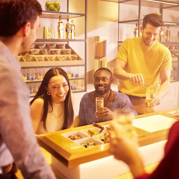 Group of friends doing the Flavour of Journey tour smiling and preparing their highball cocktails while sitting around the table with different cocktail ingredients