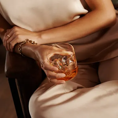 A woman holds a rocks glass of whisky and ice in her lap