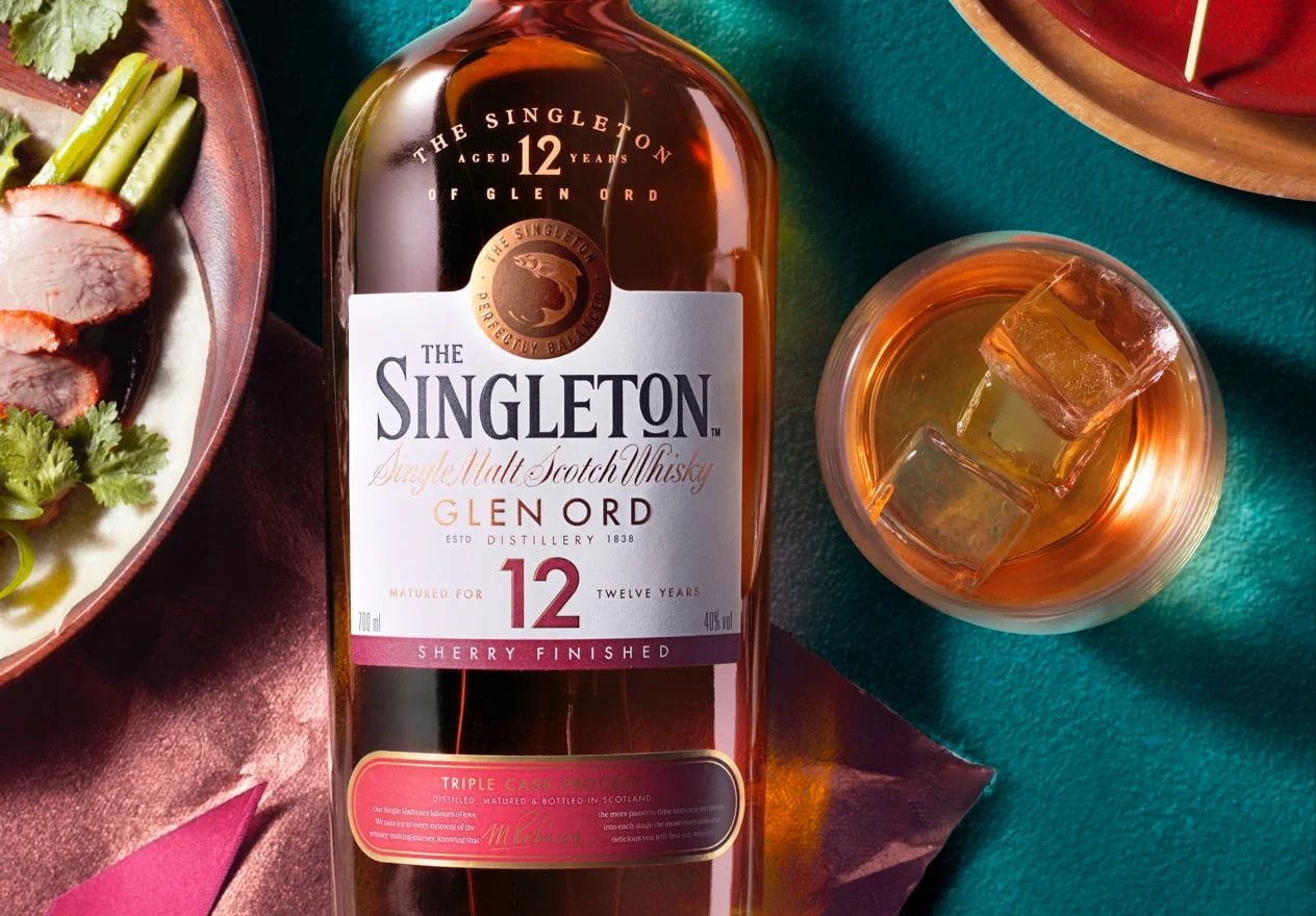 一瓶 12 年的 The Singleton Glen Ord 酒坐落在桌上，周圍環繞著一盤烤蔬菜和肉類，以及一杯威士忌。