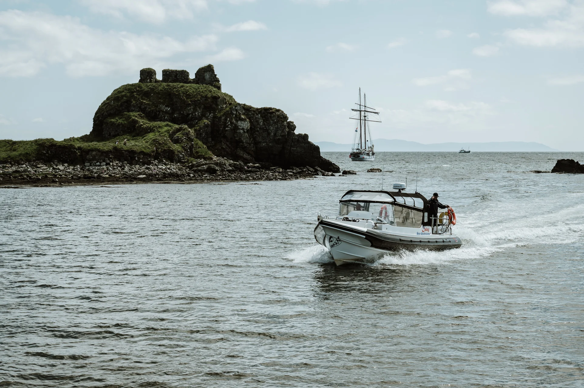 A boat sails across a body of water, with a small green island in the middle