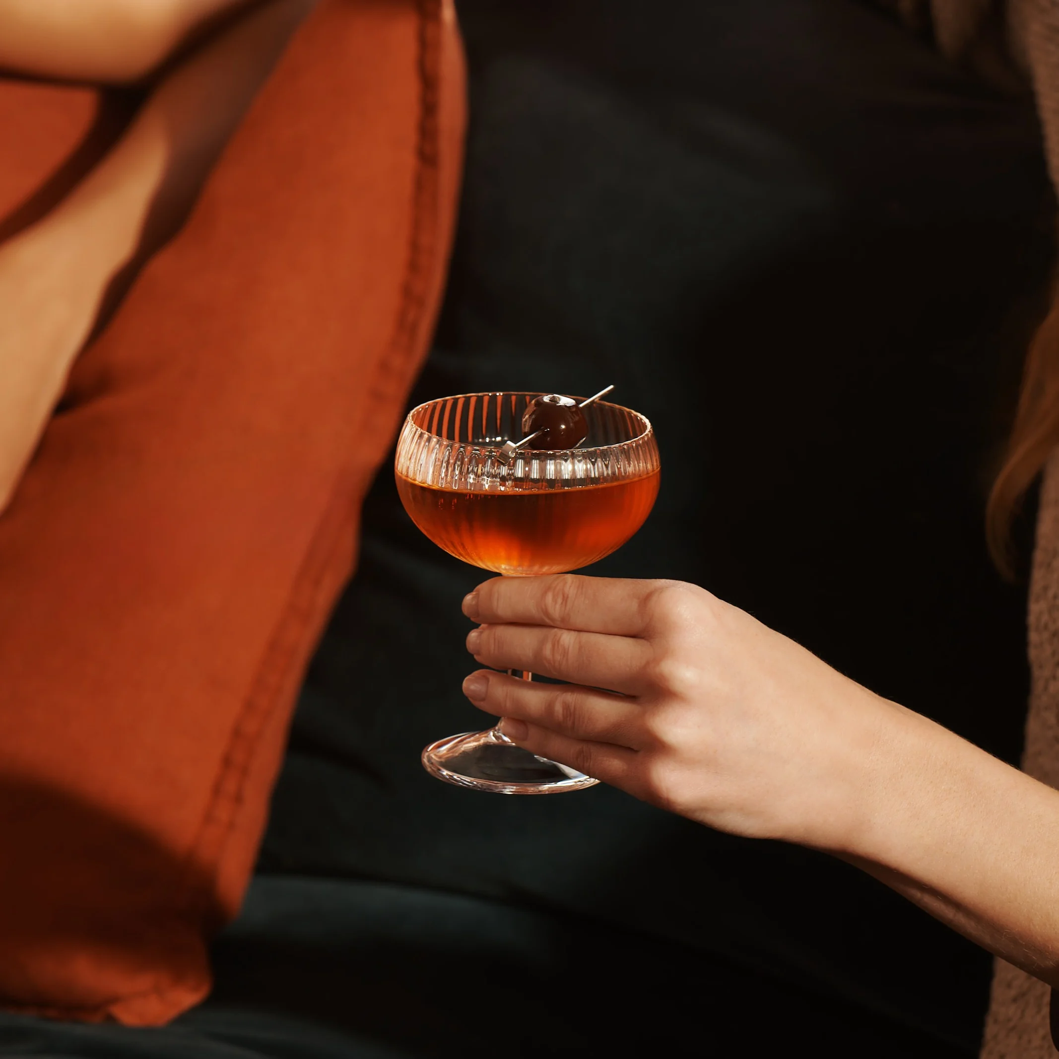 Eine Frau sitzt auf einem Sofa und hält einen Whisky-Cocktail in einem Coupé-Glas