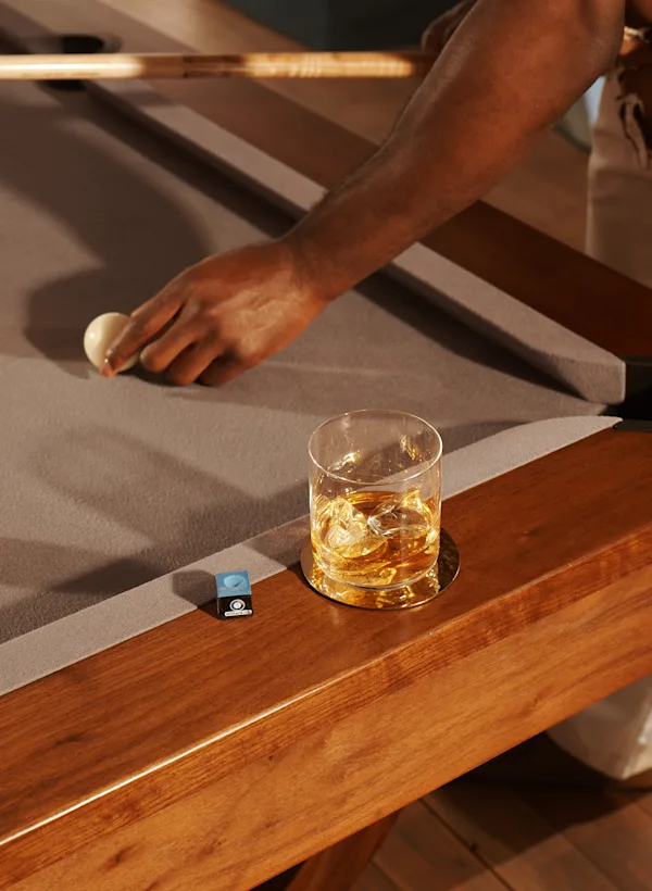 Meer informatie Een glas whisky met ijs staat op de rand van een pooltafel. Een man houdt een poolkeu vast en plaatst een witte poolbal.
