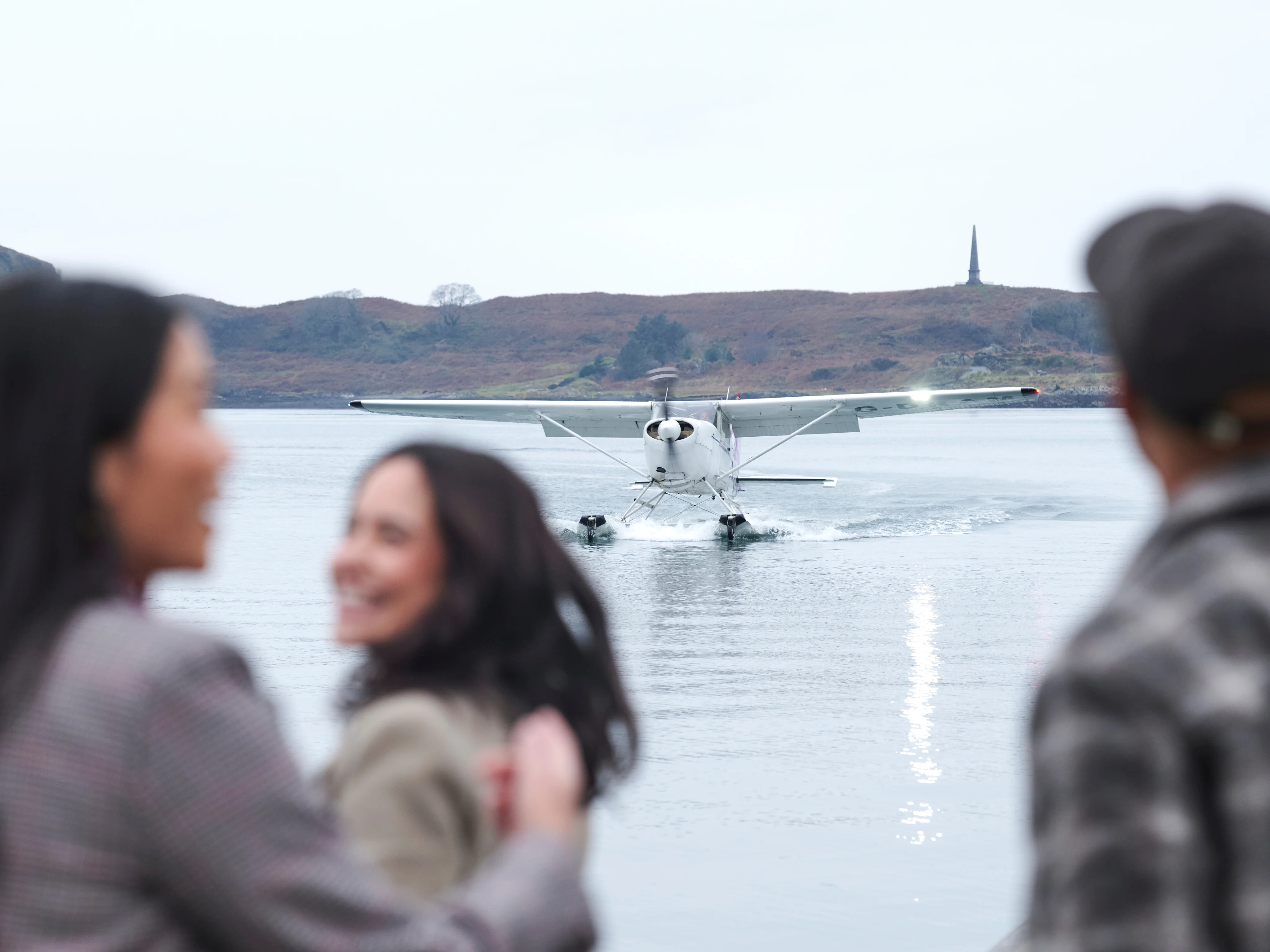 A group of smiling visitors enjoying a boat trip on the waters around the Isle of Islay, with scenic Scottish coastline visible in the background
