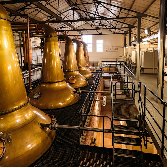 In einem Lagerhaus auf einem Balkon der Cardhu-Brennerei sind mehrere Whisky-Destilliergeräte aus Metall abgebildet.