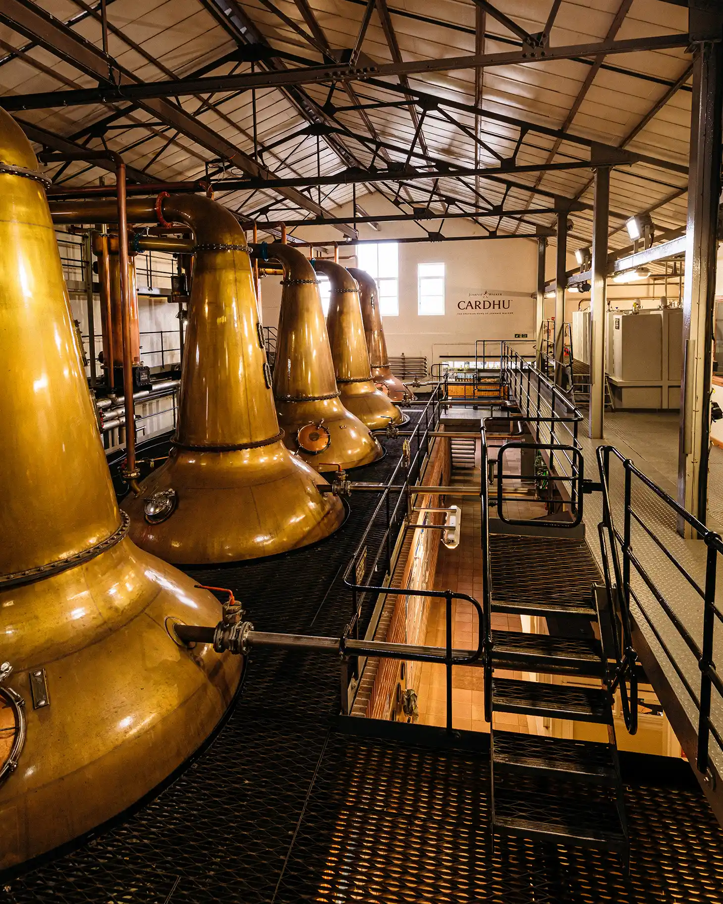 Several metal whisky stills are pictured in a warehouse on a balcony within the Cardhu distillery.