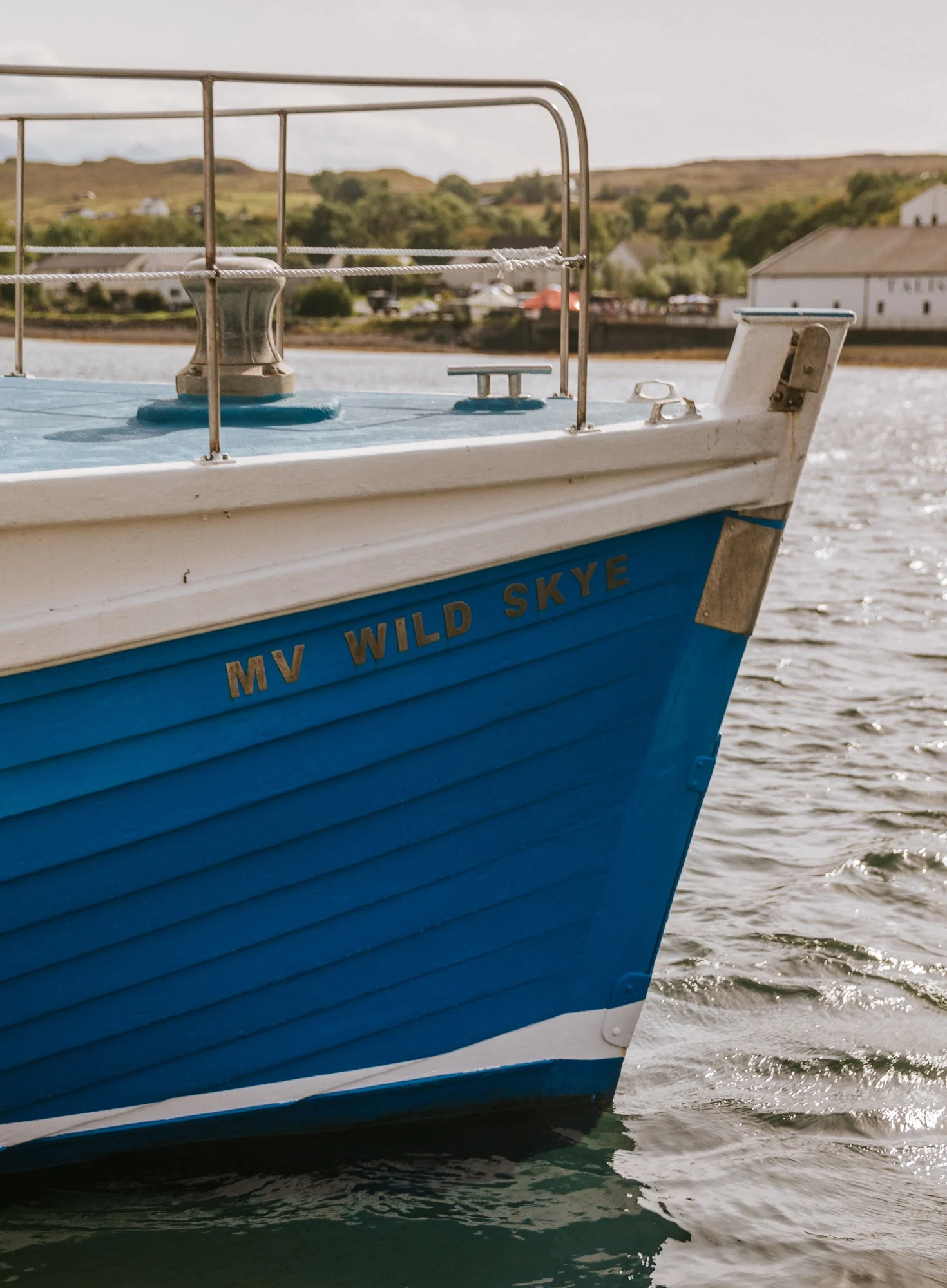 Een blauwe boot met de naam 'My Wild Skye' in het grijze water van een Schotse haven.