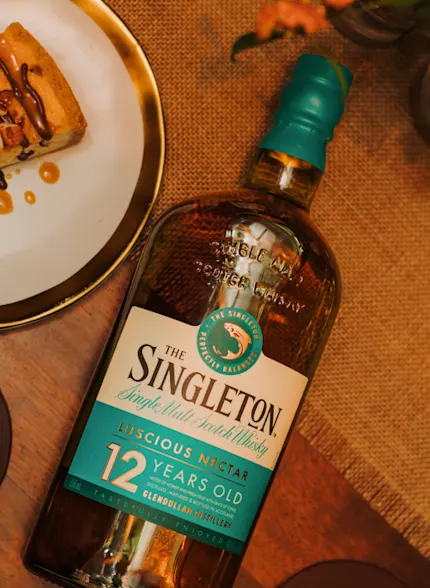 Eine Flasche des 12 Jahre alten Single Malt Scotch Whiskys von The Singleton steht auf einem Tisch neben einem Dessertteller.