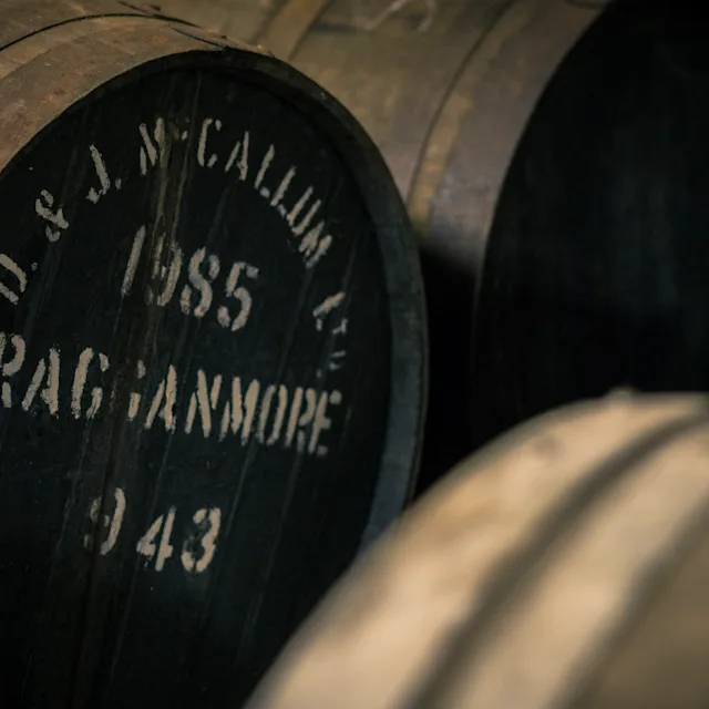 Leer meer over verschillende whiskysmaken Verschillende houten vaten staan op een rij. Op één vat staat wit op de voorkant geschreven: 'D&J McCallum, 1985, Cragganmore, 943'.