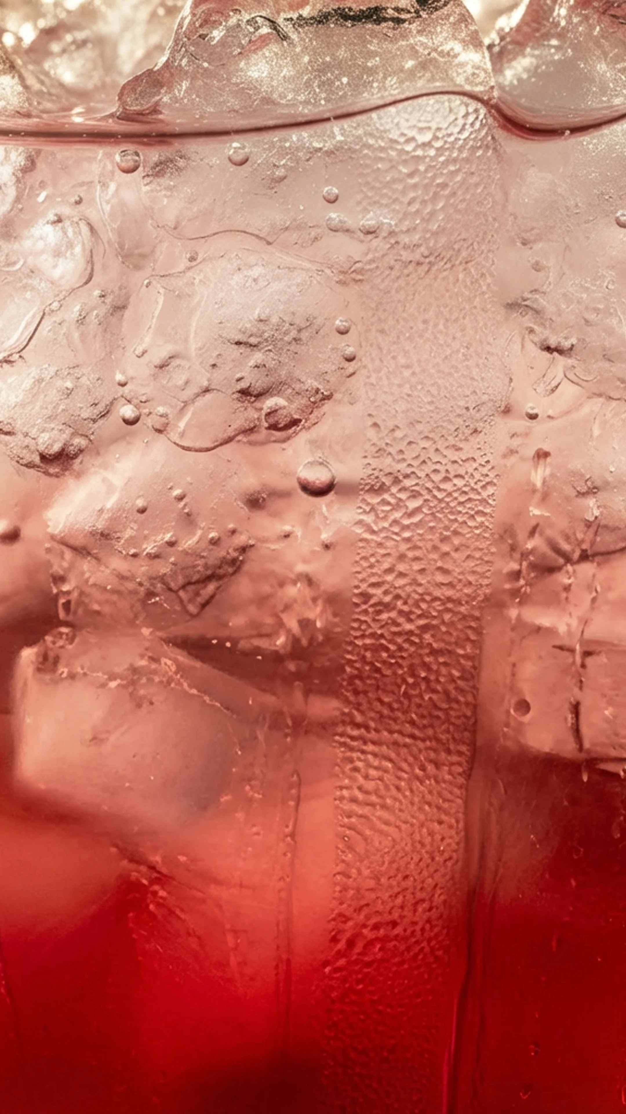 A close up of a red-purple liquid in a glass with ice and bubbles