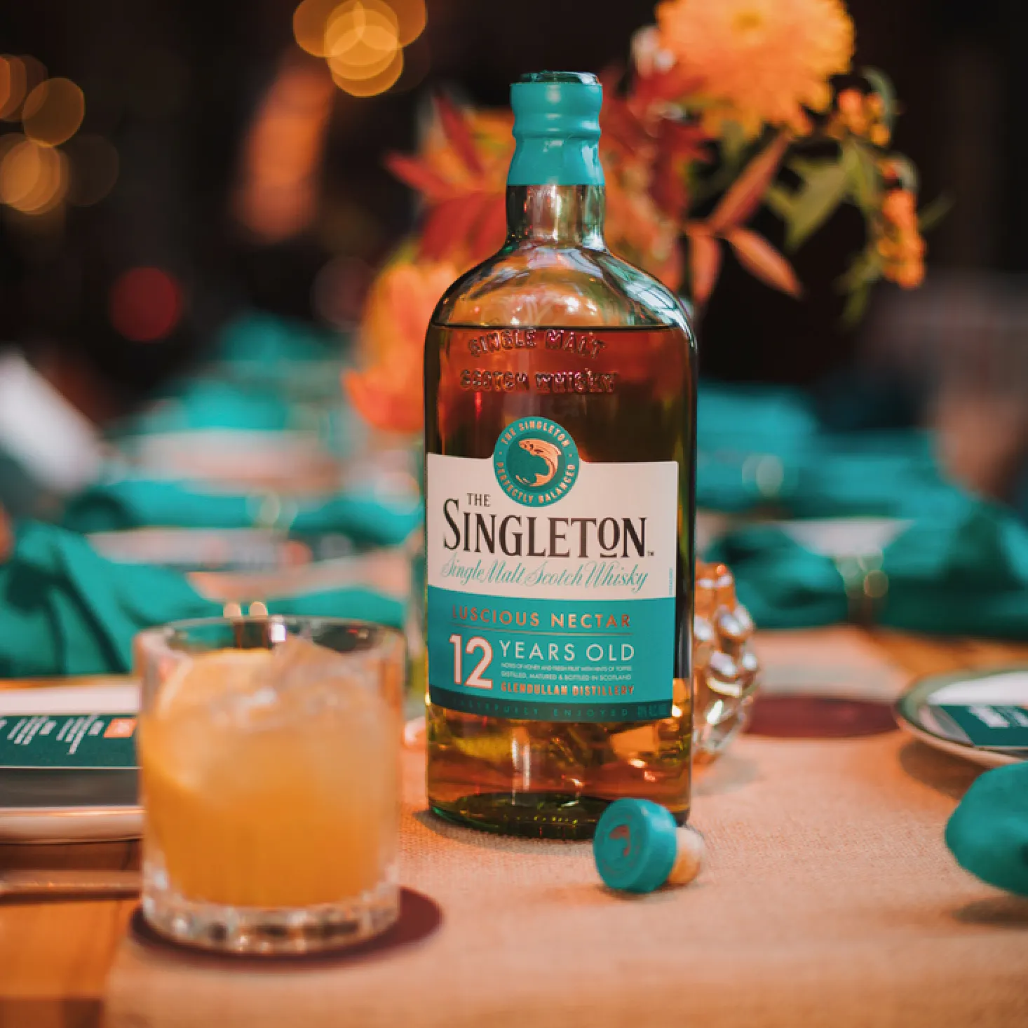 The Singleton of Dufftown 12 Year Old bottle on a table with a cocktail and floral decorations