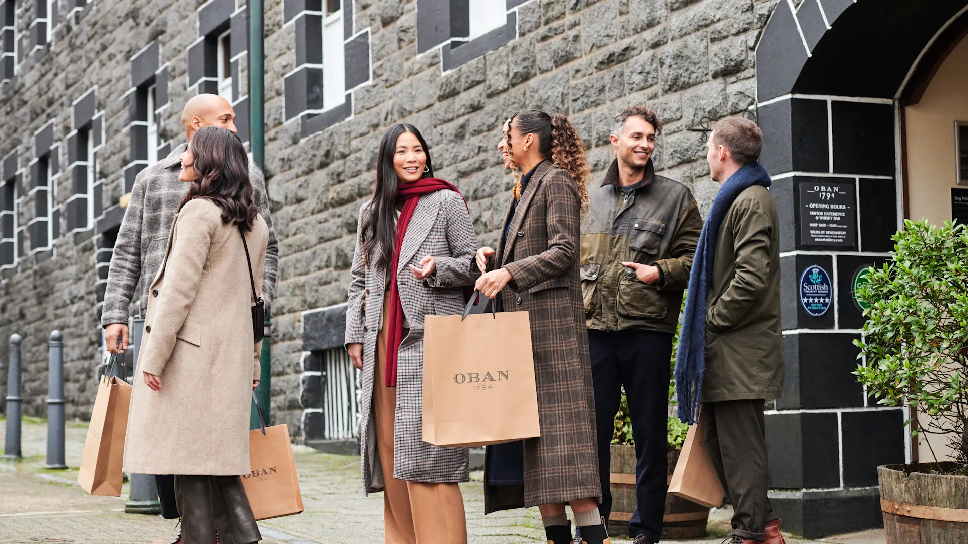 Eine Gruppe von Freunden verlässt die Oban Destillerie mit braunen Geschenktüten