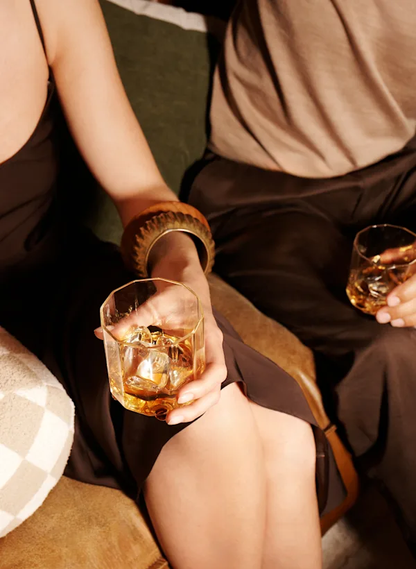 Een man en een vrouw zitten op een bank en houden glazen met whisky en ijs vast