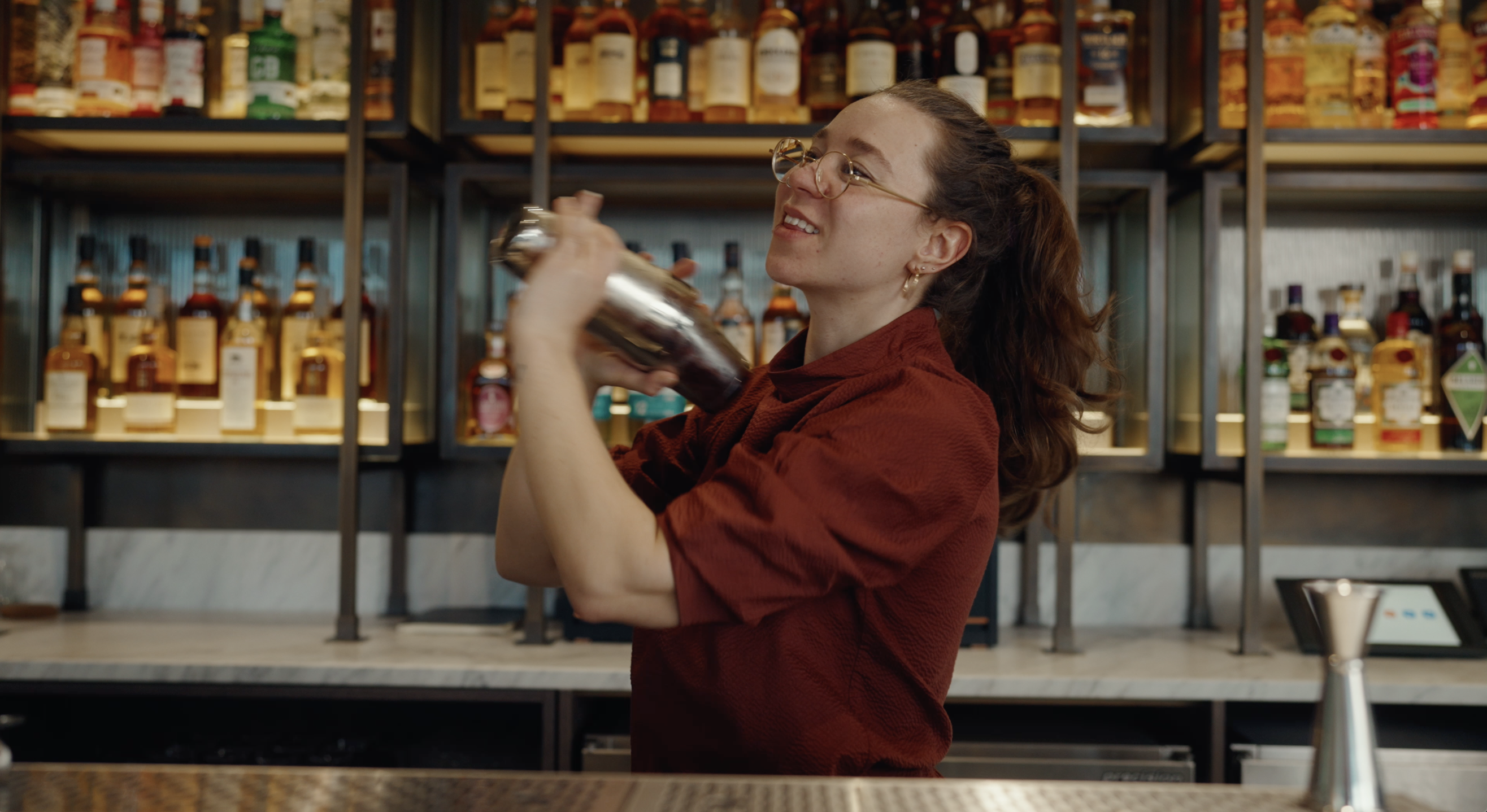 Charlotte Barker stands behind a bar, shaking a cocktail shaker