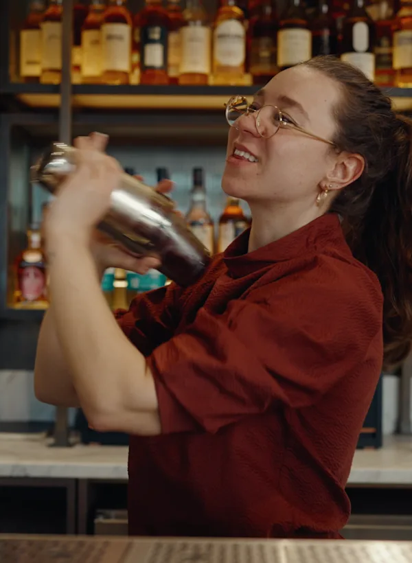 Charlotte Barker stands behind a bar, shaking a cocktail shaker