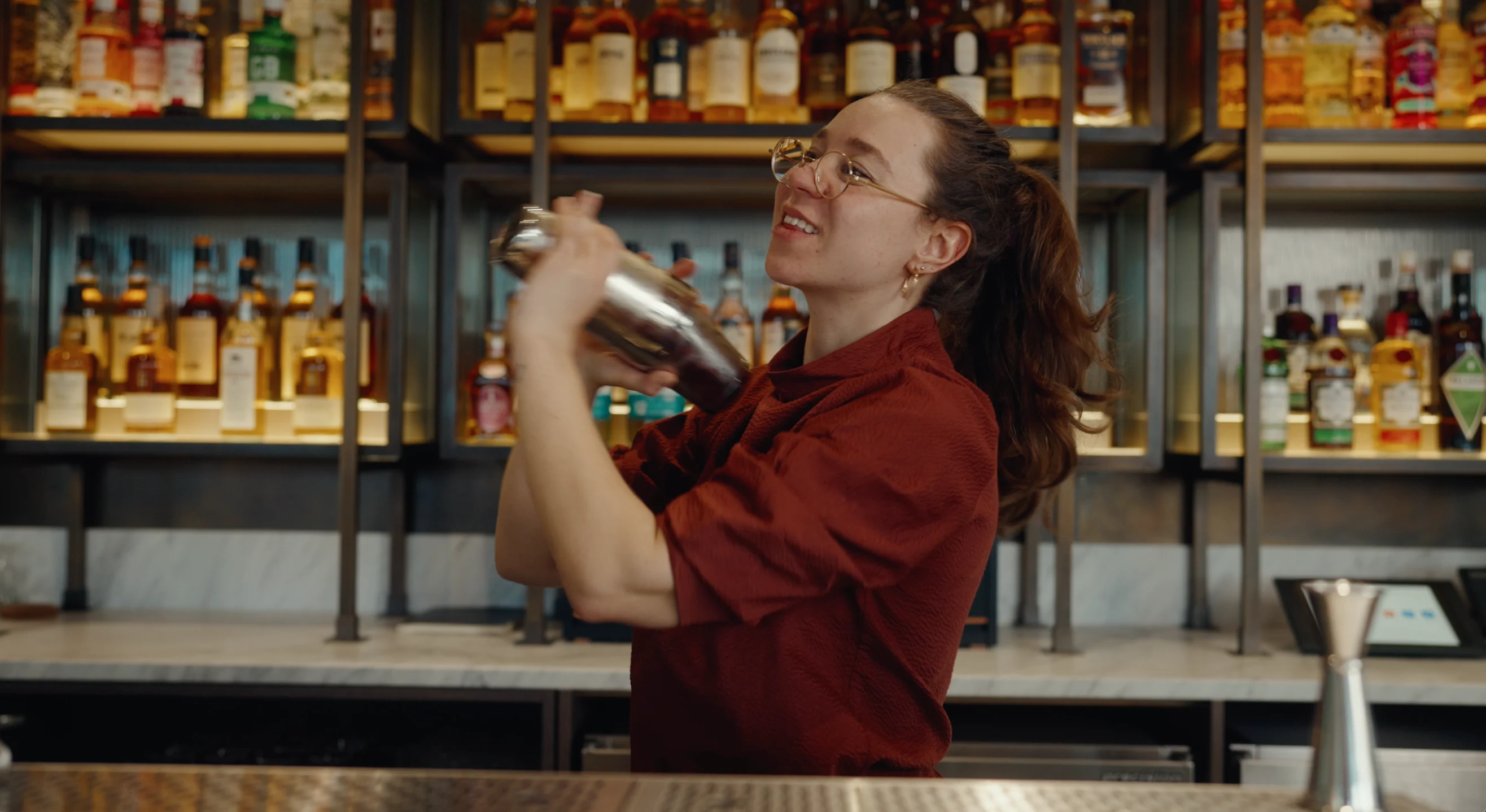 Charlotte Barker schüttelt einen Cocktail-Shaker hinter einer Bar