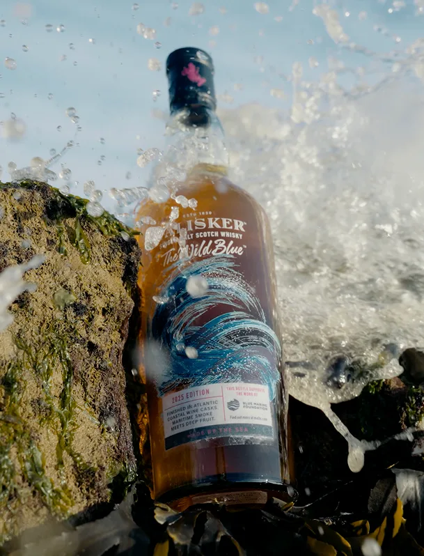 Talisker The Wild Blue whisky bottle placed on a rock with ocean waves splashing around it