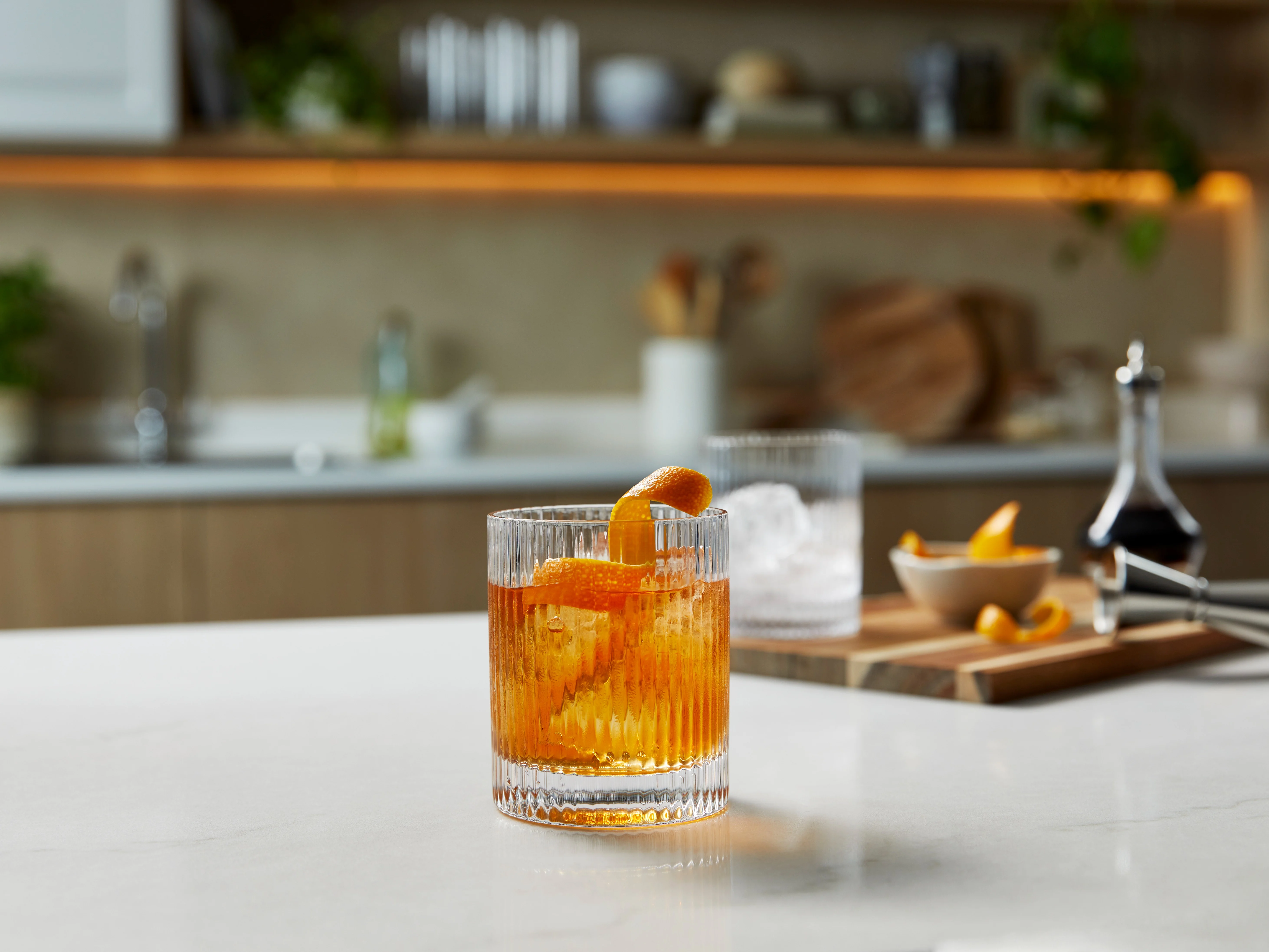 Ein Old-Fashioned-Cocktail in einem mit Eis gefüllten Eisglas mit einer Orangengarnitur.