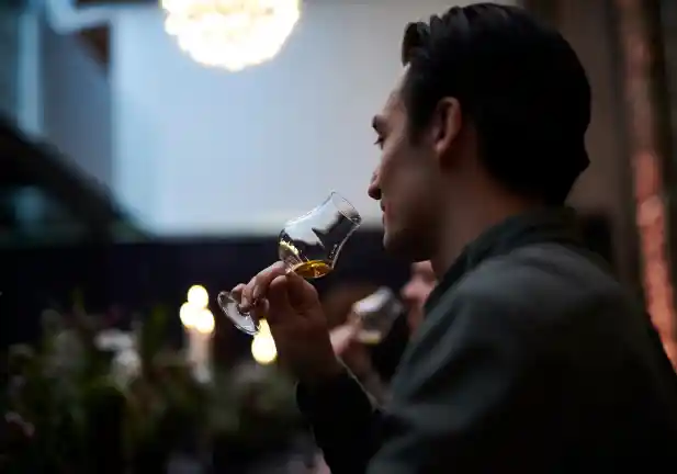 A man holds a dram glass full of whisky up to his nose.