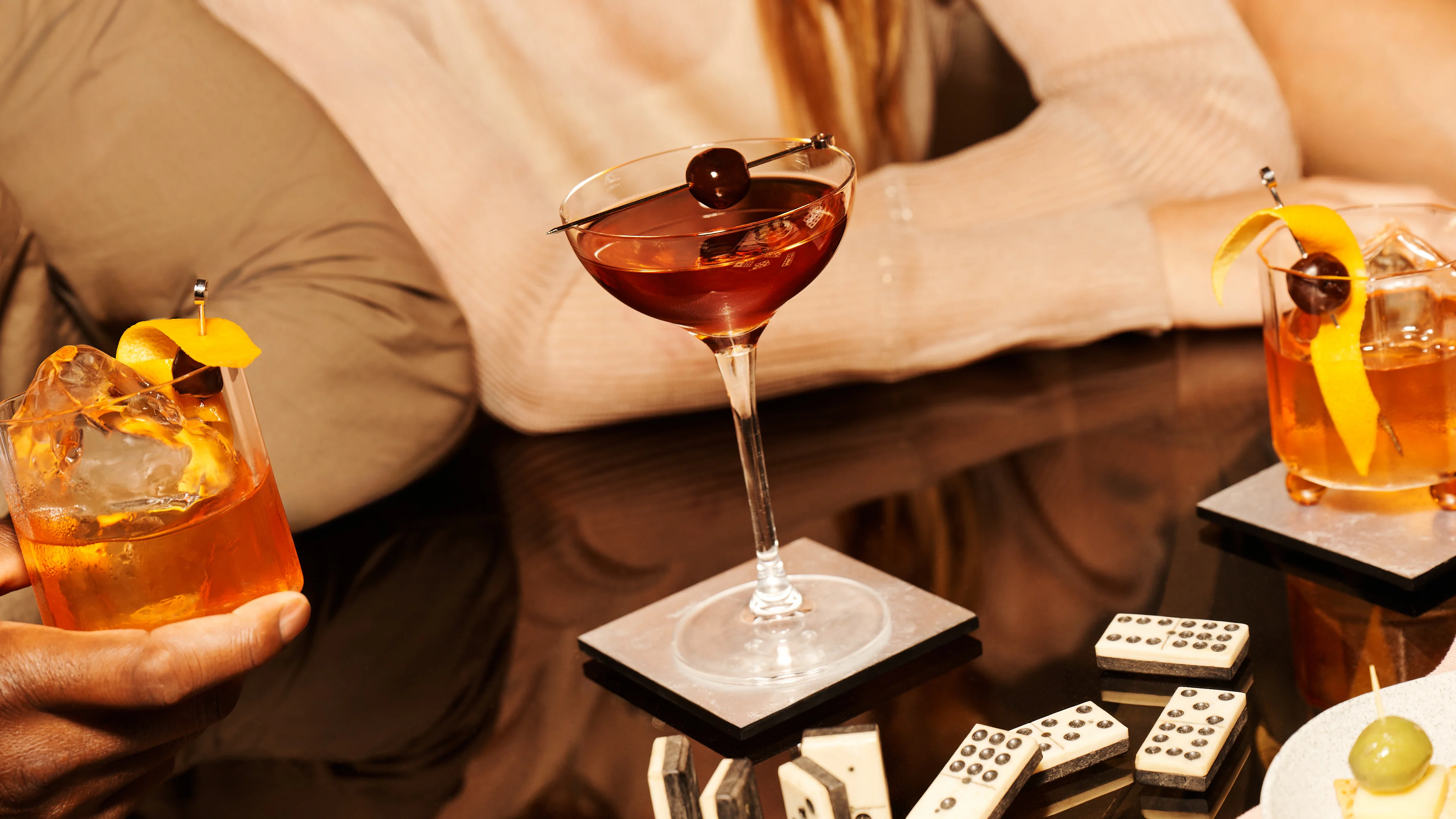 Zwei „Old Fashioned“-Cocktails und ein „Manhattan“-Cocktail auf einem Glastisch