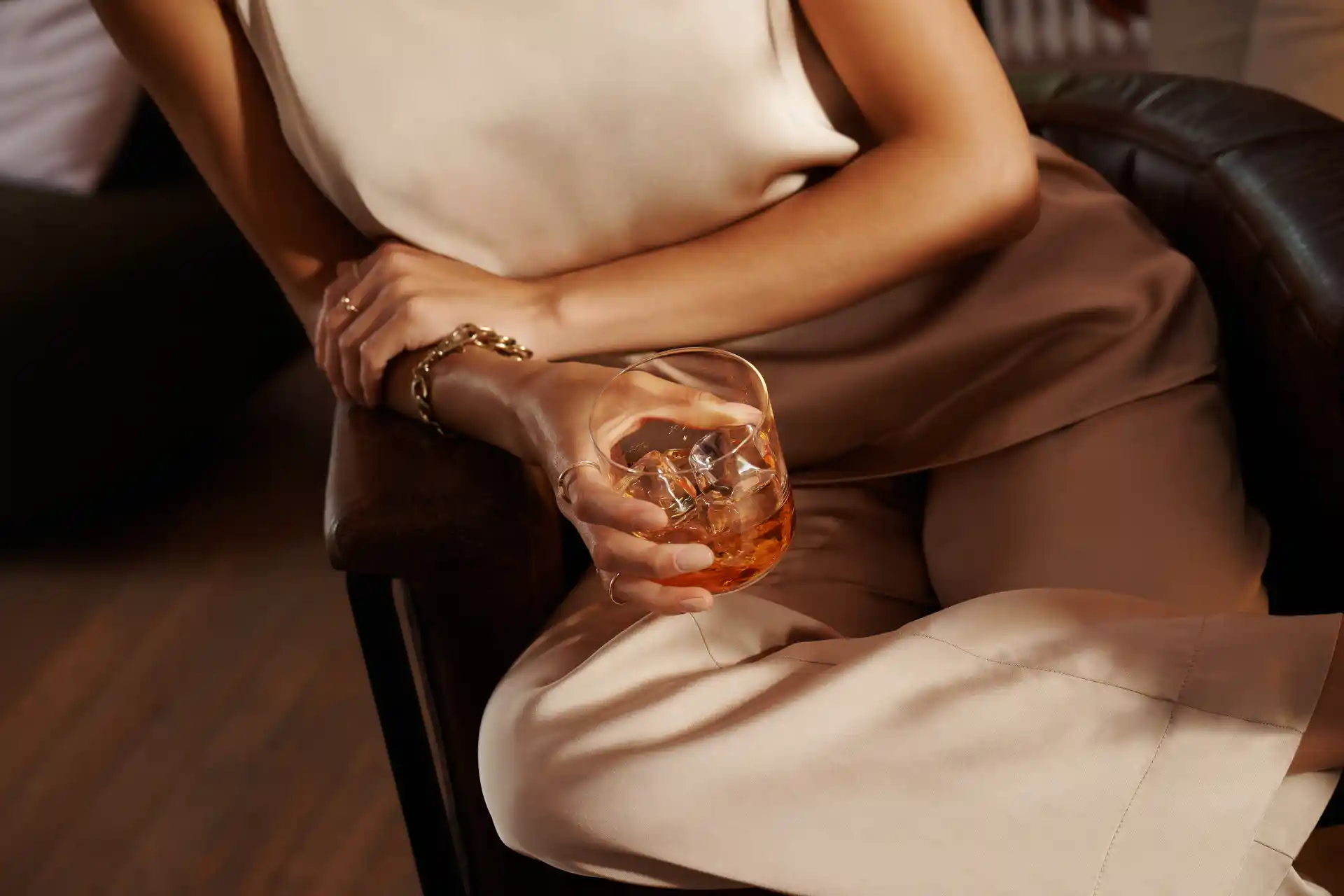 A woman holds a rocks glass containing whisky and ice in her lap