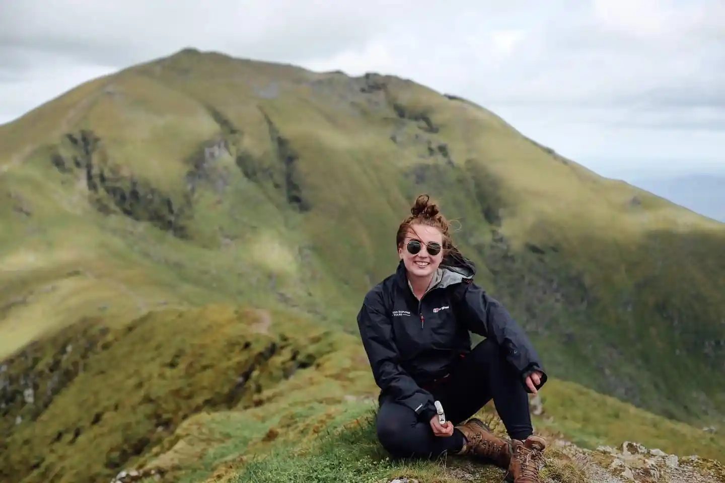 Caroline McQuistin sits atop a mountain on Isle of Skye holding a hip flask in her hands