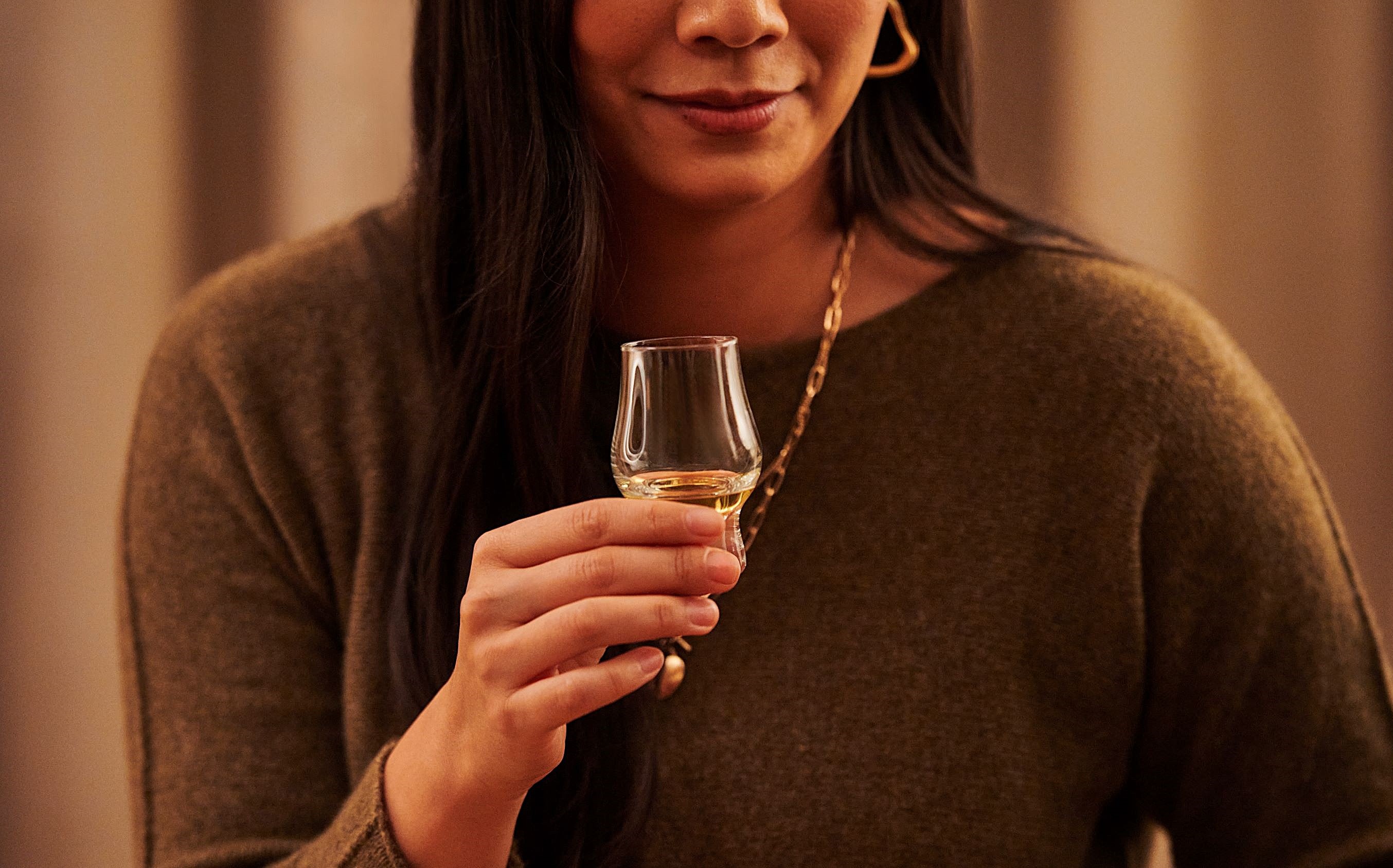 A woman holds a tulip glass containing whisky