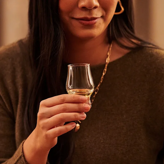 A woman holds a tulip glass containing whisky